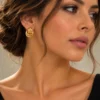 Χρυσά στρογγυλά σκουλαρίκια με καμπύλες γραμμές φορεμένα στο αυτί